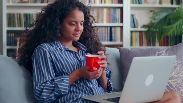 Indiano femmina guardare film su computer portatile su divano bere tè in salotto. — Video Stock