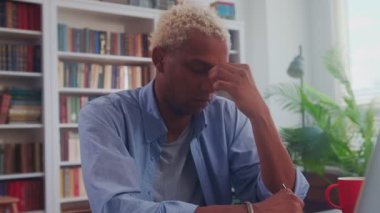 Yorgun Afro-Amerikan işadamı dizüstü bilgisayar ve buruşuk kağıtlarla kendini yorgun hissediyor