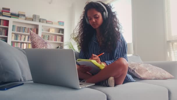 Menina adolescente indiana focada fazendo notas enquanto ouve palestras on-line. — Vídeo de Stock