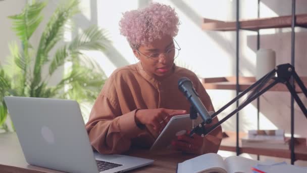 Mujer frente a un micrófono lee en una tableta digital durante un podcast. — Vídeo de stock