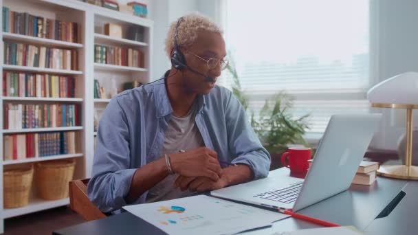 Ernstige donkere man praat op de headset en maakt notities in documenten. — Stockvideo