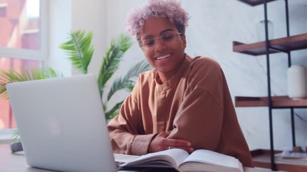 Glad attraktiv ung afro amerikansk kvinna sitter vid laptop ler mot kameran. — Stockvideo