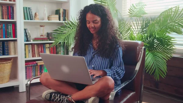 Jonge moderne Indiase vrouw zitten in stoel en thuis werken met behulp van laptop. — Stockfoto