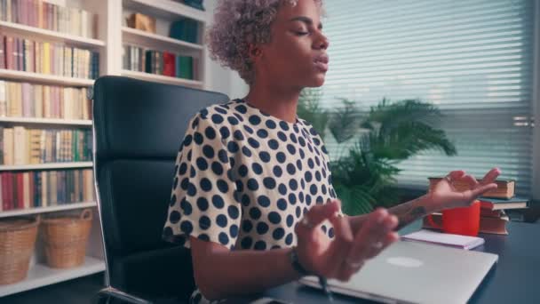 Спокойная афроамериканка с закрытыми глазами медитирует на рабочем месте — стоковое видео