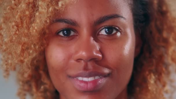 Primer plano de la cara de la mujer afroamericana que está sonriendo mirando a la cámara. — Vídeo de stock