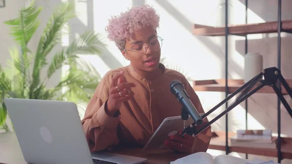 Mikrofonun önündeki kadın podcast sırasında dijital tabletten okuyor.. Stok Fotoğraf