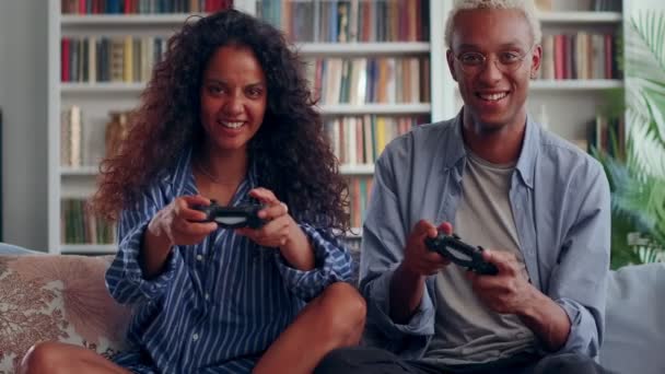 Millennial pár držení regulátory hrát videohry sedět na gauči uvnitř — Stock video