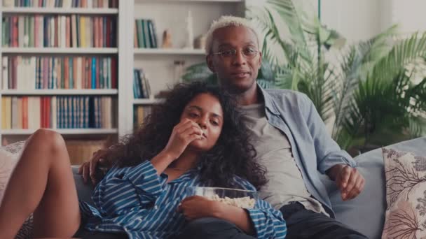 Couple Divers Rire Regarder la télévision et manger du maïs soufflé assis sur le canapé à la maison — Video