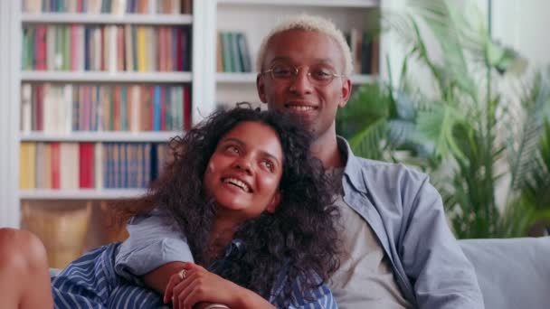 Ευτυχισμένος μελαχρινός σύζυγος και Ινδή γυναίκα στον καναπέ αγκαλιά αγκαλιά κοίτα την κάμερα — Αρχείο Βίντεο