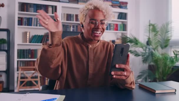 Joven mujer africana alegre hacer videollamada respuesta en el teléfono en la oficina en casa — Vídeos de Stock