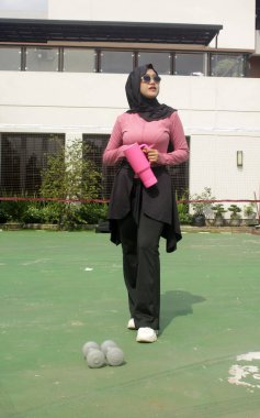 Genç Asyalı Müslüman kadın tesettür takıyor ve parkta mineral pembe şişe tutuyor.