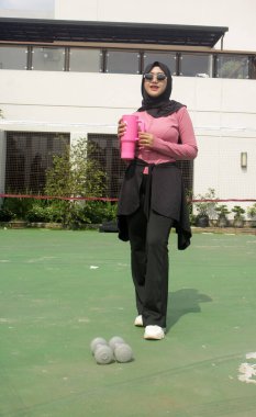 Genç Asyalı Müslüman kadın tesettür takıyor ve parkta mineral pembe şişe tutuyor.