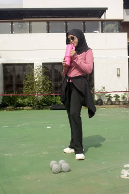 Genç Asyalı Müslüman kadın tesettür takıyor ve parkta mineral pembe şişe tutuyor.