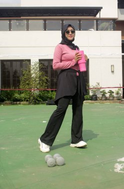 Genç Asyalı Müslüman kadın tesettür takıyor ve parkta mineral pembe şişe tutuyor.