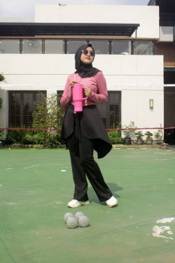 Genç Asyalı Müslüman kadın tesettür takıyor ve parkta mineral pembe şişe tutuyor.