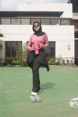 Genç Asyalı Müslüman kadın tesettür takıyor ve parkta mineral pembe şişe tutuyor.