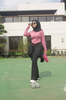 Genç Asyalı Müslüman kadın tesettür takıyor ve parkta mineral pembe şişe tutuyor.