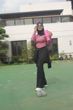 Genç Asyalı Müslüman kadın tesettür takıyor ve parkta mineral pembe şişe tutuyor.