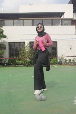 Genç Asyalı Müslüman kadın tesettür takıyor ve parkta mineral pembe şişe tutuyor.