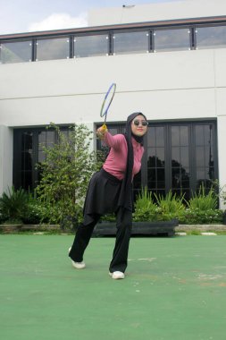 Müslüman kadın parkta badminton oynuyor.