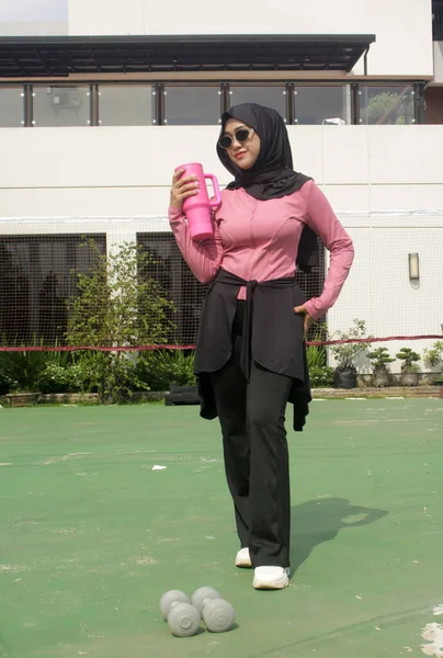 Genç Asyalı Müslüman kadın tesettür takıyor ve parkta mineral pembe şişe tutuyor.