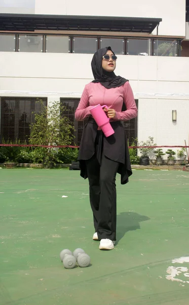 Genç Asyalı Müslüman kadın tesettür takıyor ve parkta mineral pembe şişe tutuyor.