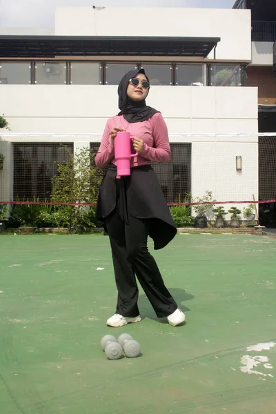 Genç Asyalı Müslüman kadın tesettür takıyor ve parkta mineral pembe şişe tutuyor.