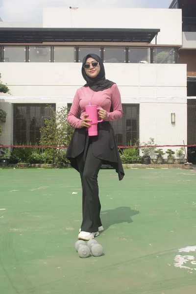 Genç Asyalı Müslüman kadın tesettür takıyor ve parkta mineral pembe şişe tutuyor.