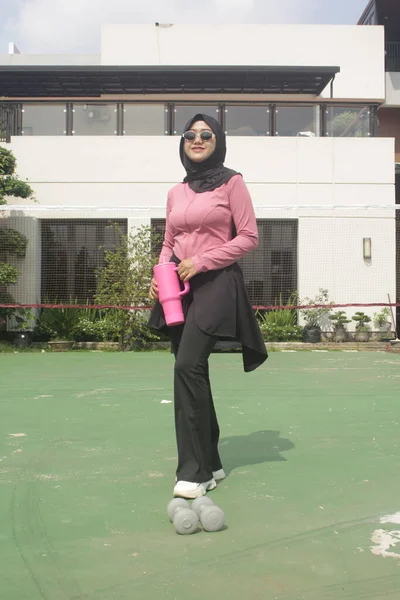 Genç Asyalı Müslüman kadın tesettür takıyor ve parkta mineral pembe şişe tutuyor.