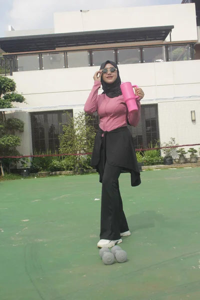 Genç Asyalı Müslüman kadın tesettür takıyor ve parkta mineral pembe şişe tutuyor.