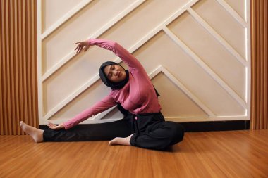 Genç bir kadın spor salonunda esneme hareketleri yapıyor.