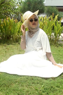 Genç Asyalı kadın tesettür takıyor parktaki çimlerde dinleniyor..