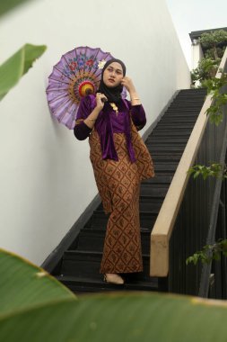 Geleneksel elbiseli Asyalı Müslüman kadın geleneksel evde geleneksel Malay elbisesi giyiyor. Geleneksel bayram kutlamaları sırasında geleneksel Malay kadını