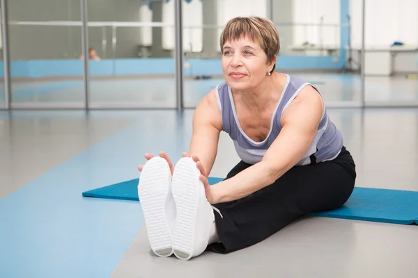 Äldre kvinna gör stretching övningar i gym — Stockfoto