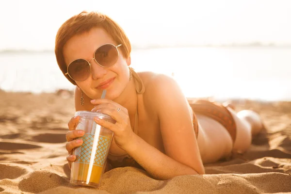 Dívka s nápojem sunbathes na pláži — Stock fotografie