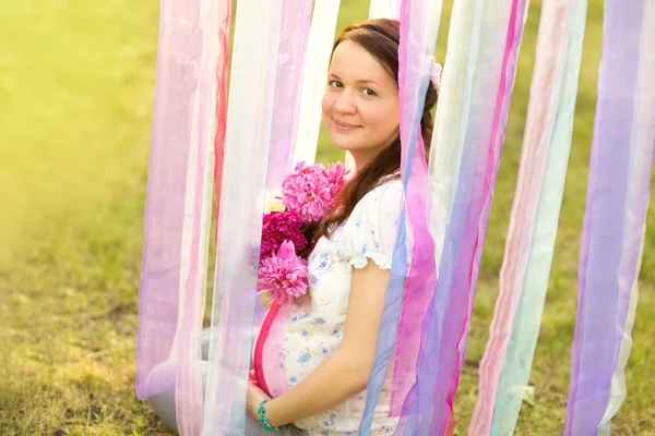 Hermosa mujer embarazada con un ramo de flores relajándose fuera en el parque —  Fotos de Stock