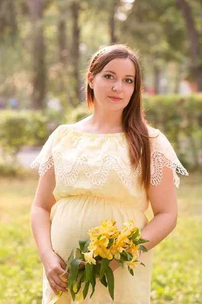 The young beautiful pregnant woman with flowers in park in summer day — Stock Photo, Image