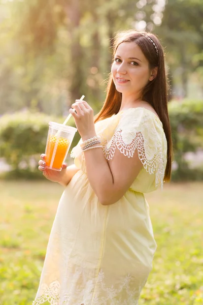 A bela mulher grávida jovem com suco no parque no dia de verão — Fotografia de Stock