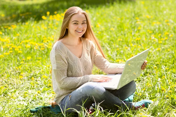 A mulher jovem com o computador portátil em uma grama no parque — Fotografia de Stock