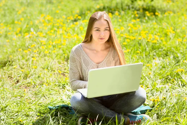 A mulher jovem com o computador portátil em uma grama no parque — Fotografia de Stock