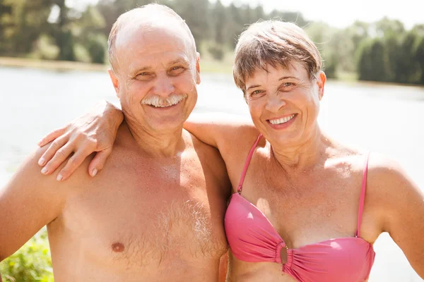 the elderly laughing couple on the beach looks in the camera