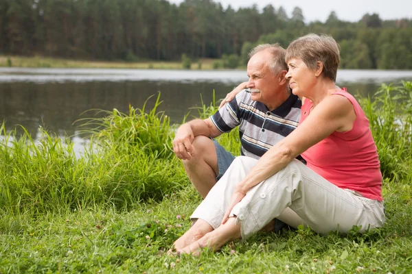 Feliz pareja de ancianos sentados en verano cerca del lago — Foto de Stock