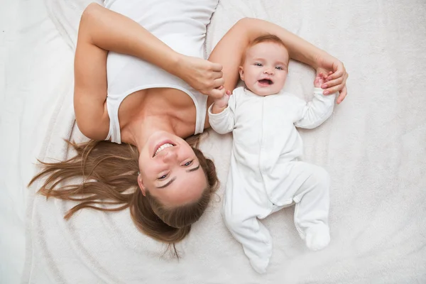 Madre e hijo en una cama blanca. Mamá y el bebé en pañal jugando en el dormitorio soleado . — Foto de Stock