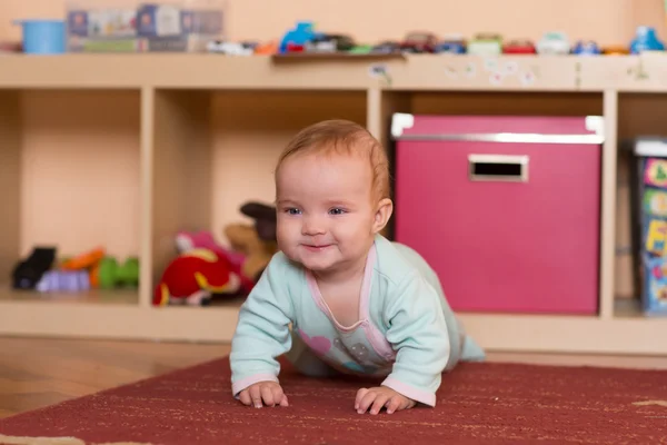 Baby spela och kryper, göra grimaser, på golvet. — Stockfoto