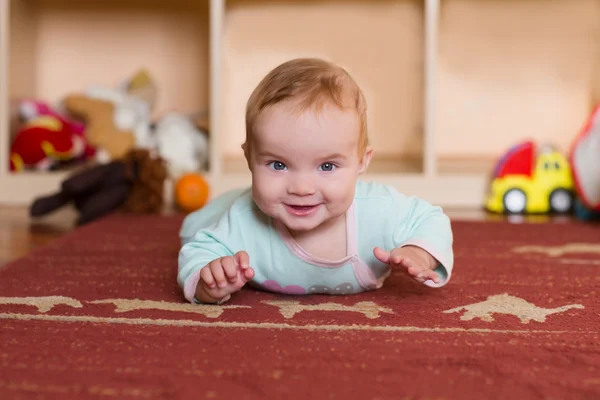 Baby spela och kryper, göra grimaser, på golvet. — Stockfoto