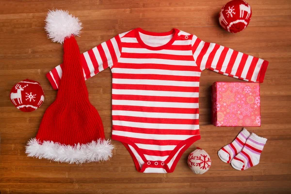 Vêtements de Noël bébé avec bijoux de Noël sur fond en bois. Père Noël bébé vêtements isolésisolées. Ensemble de vêtements pour enfants Noël . — Photo