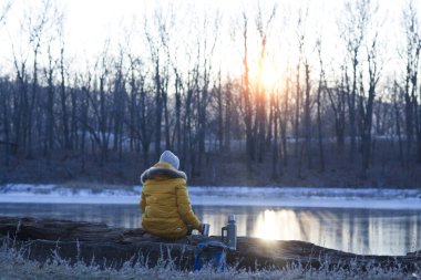 Genç bir kadın kış ormanında kahve içiyor..