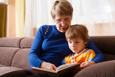 Büyükannem ve torunum evde kanepede otururken kitap okuyorlar.