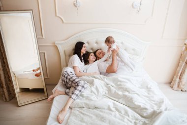 Genç mutlu ebeveynler ve kızları yatakta yatarken birlikte oynuyorlar, aile zamanı konsepti. 