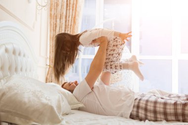 Genç mutlu baba ve kızı yatakta yatarken birlikte oynuyorlar, aile zamanı konsepti. 